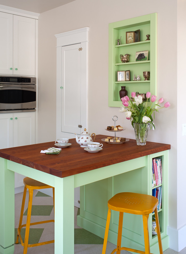 Inspiration for a mid-sized traditional l-shaped eat-in kitchen in San Diego with linoleum floors, a farmhouse sink, shaker cabinets, green cabinets, wood benchtops, green splashback, subway tile splashback, stainless steel appliances, a peninsula and green floor.
