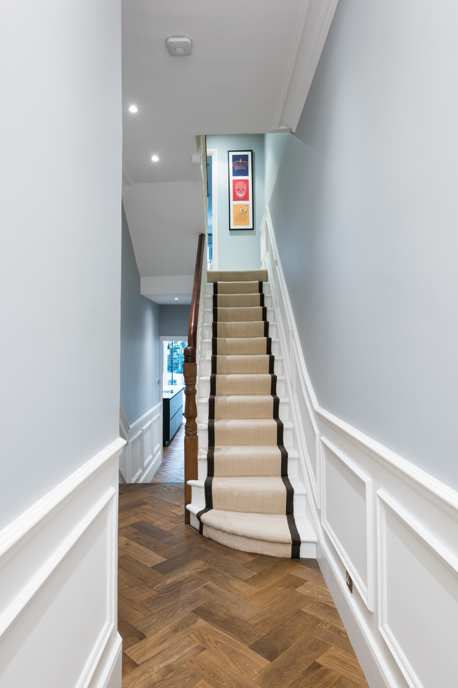 Photo of a mid-sized traditional carpeted straight staircase in London with carpet risers and wood railing.