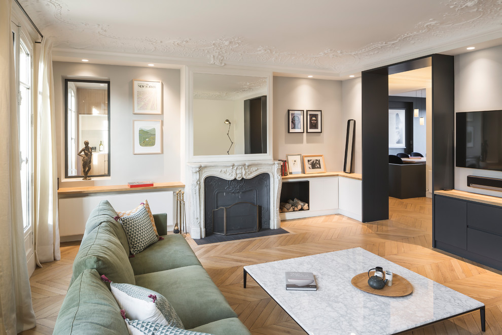 This is an example of a large contemporary enclosed living room in Paris with grey walls, light hardwood floors, a standard fireplace, a wall-mounted tv, a metal fireplace surround and brown floor.