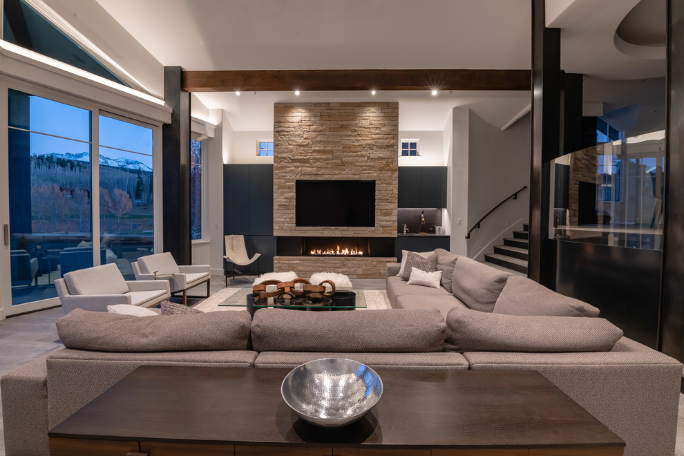 Large contemporary open concept living room in Denver with a home bar, grey walls, a standard fireplace, a stone fireplace surround, a wall-mounted tv and grey floor.