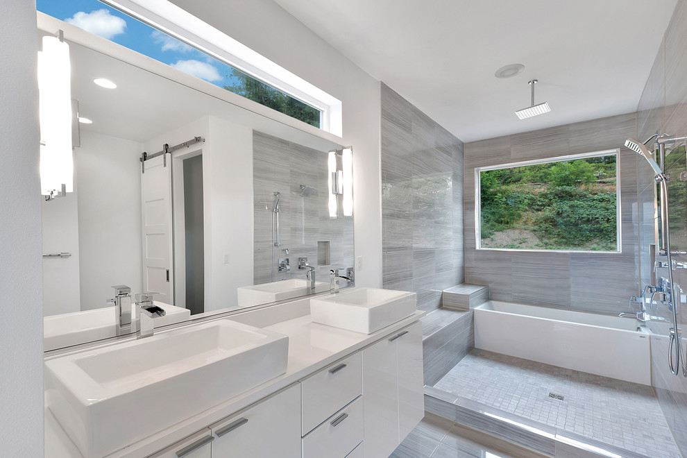 Photo of a mid-sized modern master bathroom in Seattle with a vessel sink, flat-panel cabinets, white cabinets, engineered quartz benchtops, an alcove tub, a shower/bathtub combo, gray tile, porcelain tile, white walls and porcelain floors.