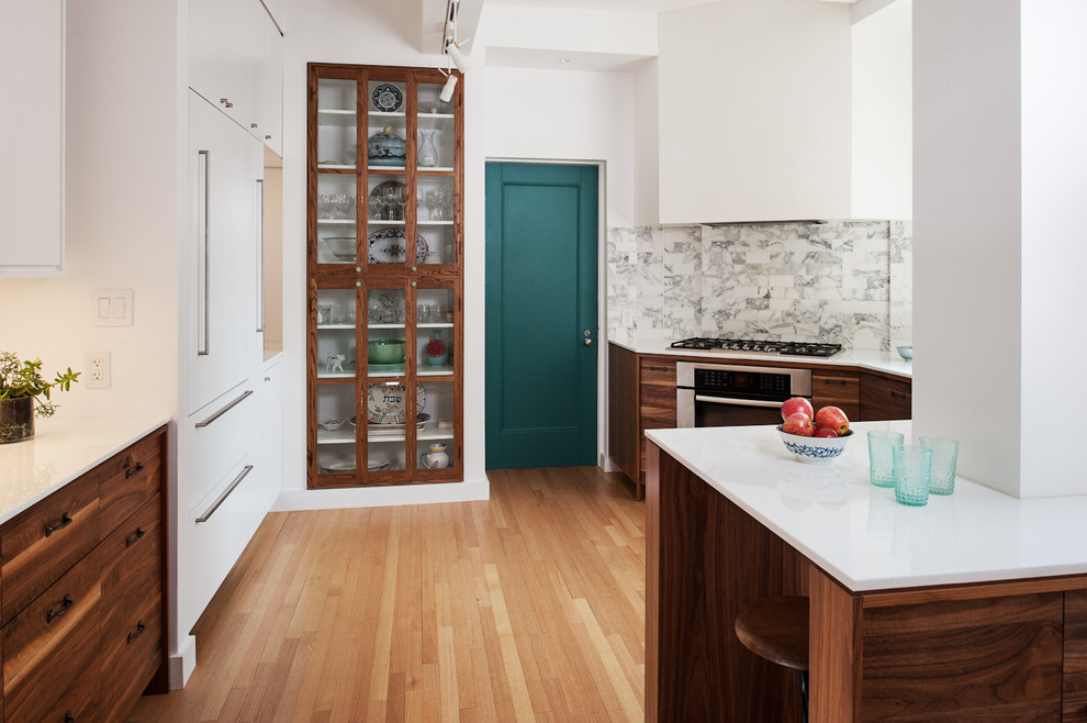 This is an example of a modern u-shaped eat-in kitchen in New York with an undermount sink, flat-panel cabinets, medium wood cabinets, glass benchtops, white splashback, stone tile splashback, panelled appliances, light hardwood floors and a peninsula.