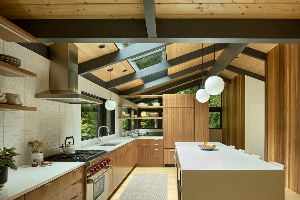 Photo of a midcentury l-shaped eat-in kitchen in Portland with a drop-in sink, medium wood cabinets, quartz benchtops, white splashback, subway tile splashback, stainless steel appliances, light hardwood floors, with island, white benchtop, exposed beam, flat-panel cabinets and brown floor.