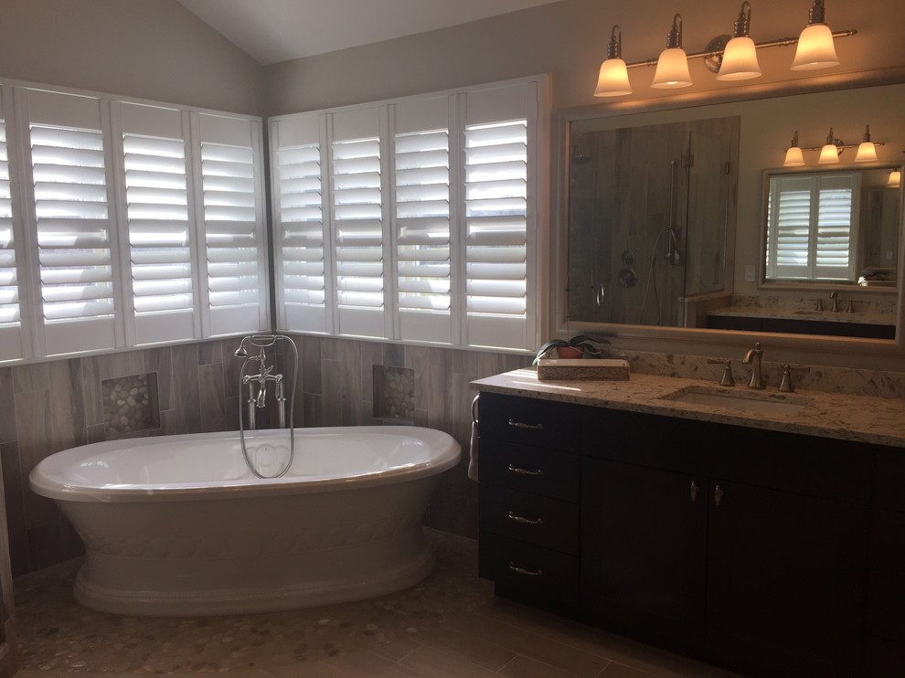 Large transitional master gray tile and porcelain tile light wood floor and brown floor freestanding bathtub photo in Baltimore with shaker cabinets, dark wood cabinets, a two-piece toilet, beige walls, an undermount sink, solid surface countertops and a hinged shower door