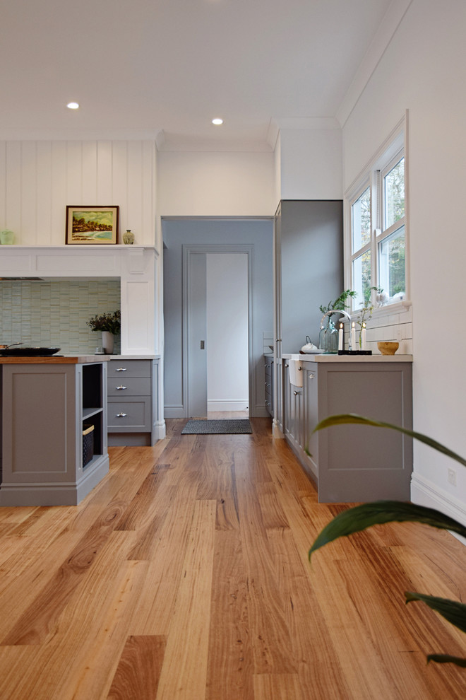 Design ideas for a large traditional galley open plan kitchen in Melbourne with a farmhouse sink, shaker cabinets, grey cabinets, wood benchtops, green splashback, ceramic splashback, stainless steel appliances, light hardwood floors and with island.