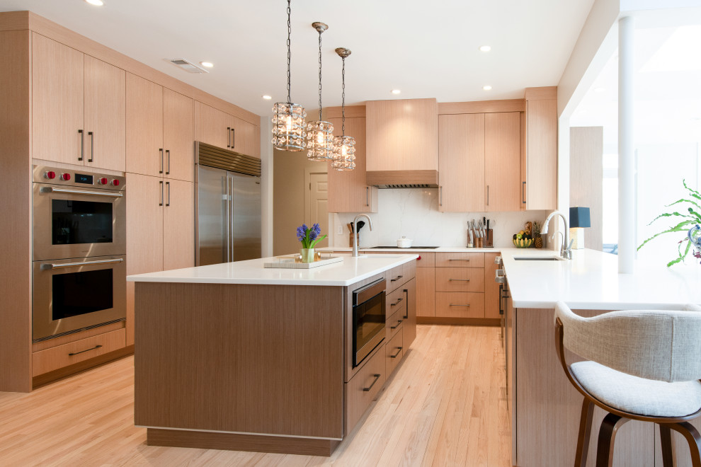 Trendy u-shaped light wood floor and beige floor kitchen photo in DC Metro with an undermount sink, flat-panel cabinets, light wood cabinets, white backsplash, stainless steel appliances, an island and white countertops