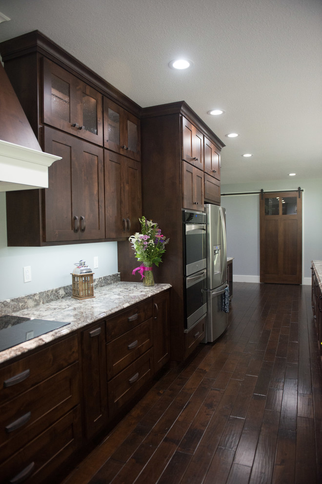 Example of a transitional l-shaped open concept kitchen design with an undermount sink, shaker cabinets, dark wood cabinets, granite countertops, stainless steel appliances, an island and multicolored countertops