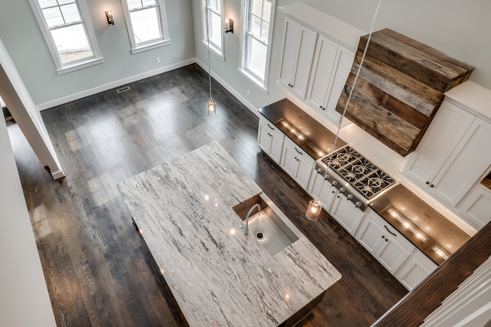 Inspiration for a mid-sized arts and crafts galley open plan kitchen in Nashville with a farmhouse sink, shaker cabinets, white cabinets, granite benchtops, white splashback, ceramic splashback, stainless steel appliances, dark hardwood floors and with island.