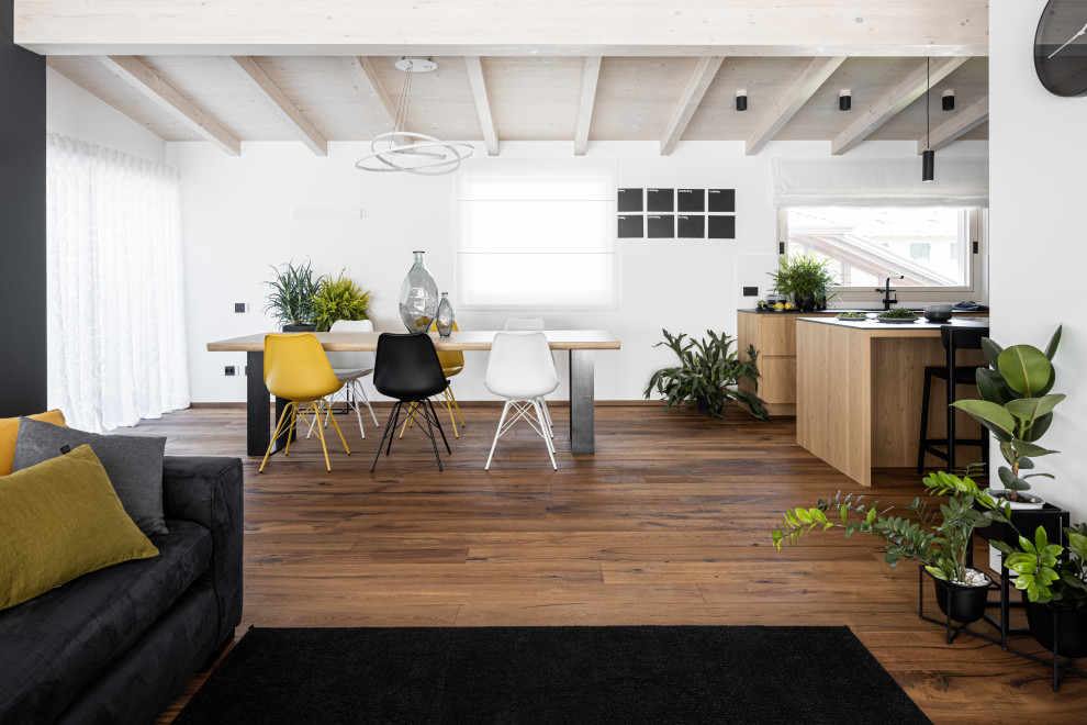 Moderne Wohnküche mit weißer Wandfarbe, dunklem Holzboden, braunem Boden und freigelegten Dachbalken in Sonstige