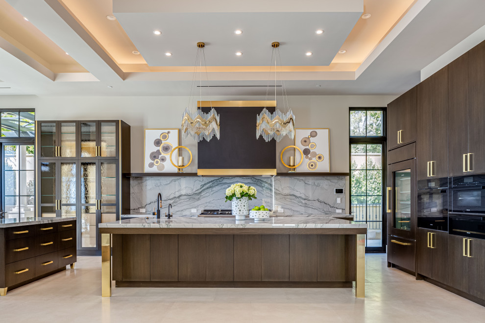 Photo of a large contemporary u-shaped eat-in kitchen in Orange County with marble benchtops, a drop-in sink, flat-panel cabinets, medium wood cabinets, grey splashback, stone slab splashback, black appliances, limestone floors, multiple islands, beige floor, grey benchtop and recessed.