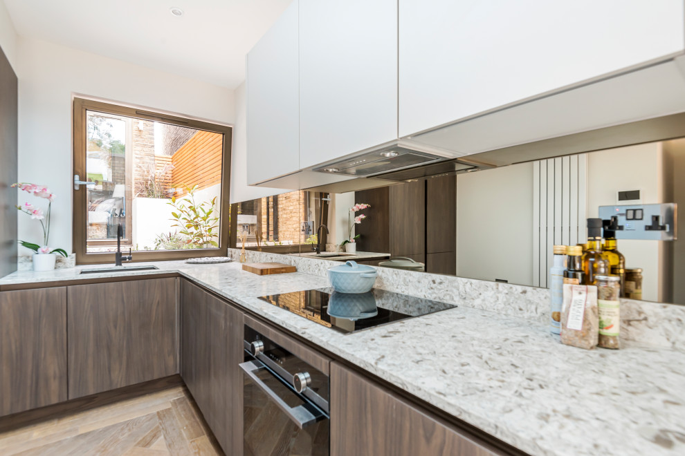 Photo of a small modern single-wall eat-in kitchen in London with a drop-in sink, flat-panel cabinets, quartzite benchtops, mirror splashback and no island.