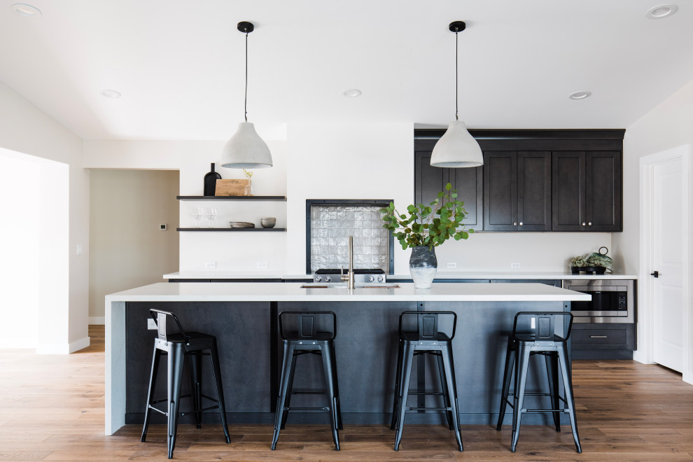 Example of a transitional galley medium tone wood floor and brown floor open concept kitchen design in Phoenix with an undermount sink, shaker cabinets, black cabinets, stainless steel appliances, an island and white countertops