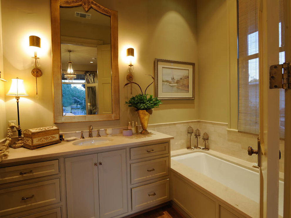 Design ideas for a small traditional master bathroom in New Orleans with shaker cabinets, grey cabinets, an undermount tub, beige tile, stone tile, beige walls, light hardwood floors, an undermount sink and solid surface benchtops.