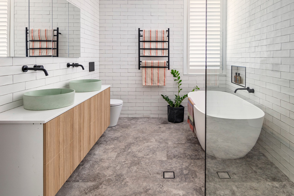 Design ideas for a beach style wet room bathroom in Sydney with a freestanding tub, flat-panel cabinets, light wood cabinets, a wall-mount toilet, white tile, white walls, a vessel sink, grey floor, an open shower and white benchtops.