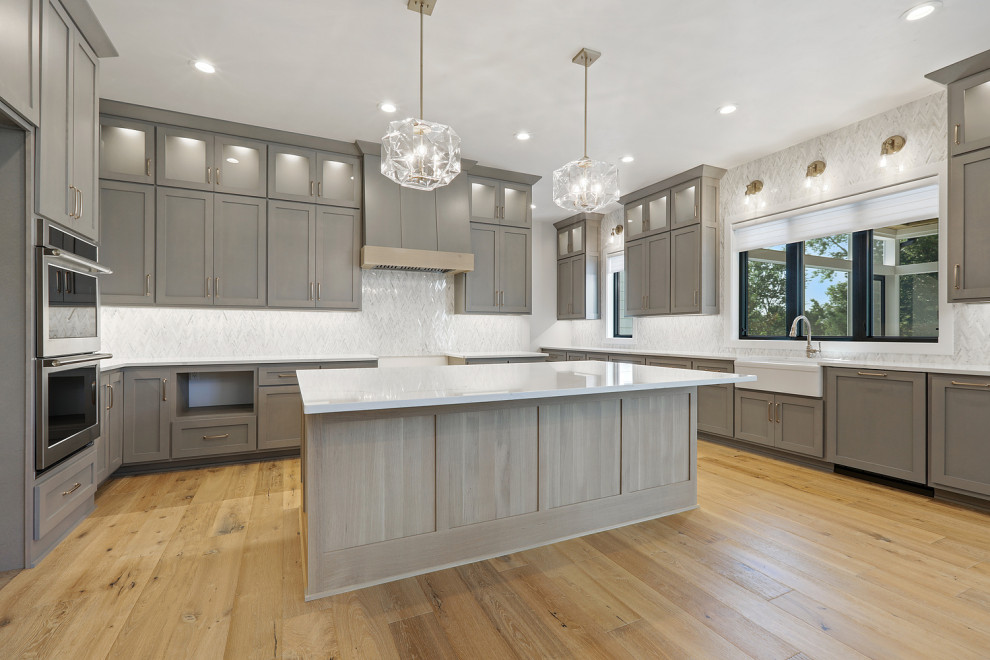 Eat-in kitchen - large transitional u-shaped light wood floor and brown floor eat-in kitchen idea with a farmhouse sink, shaker cabinets, gray cabinets, quartz countertops, multicolored backsplash, marble backsplash, stainless steel appliances, an island and white countertops