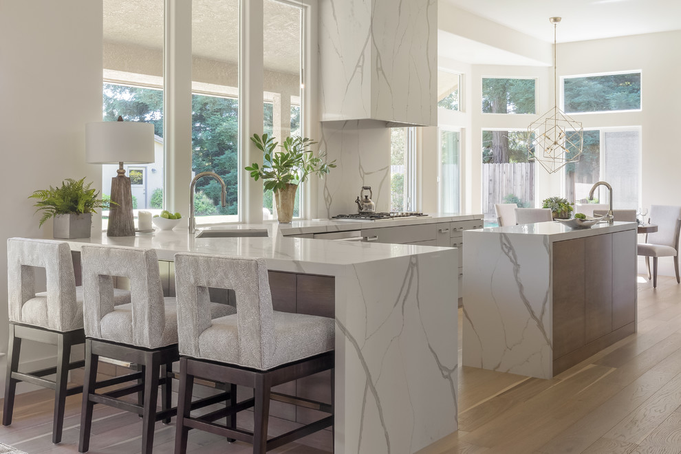 Photo of a large contemporary l-shaped eat-in kitchen in Sacramento with an undermount sink, flat-panel cabinets, grey cabinets, white splashback, stone slab splashback, light hardwood floors, with island, beige floor, white benchtop, marble benchtops and stainless steel appliances.