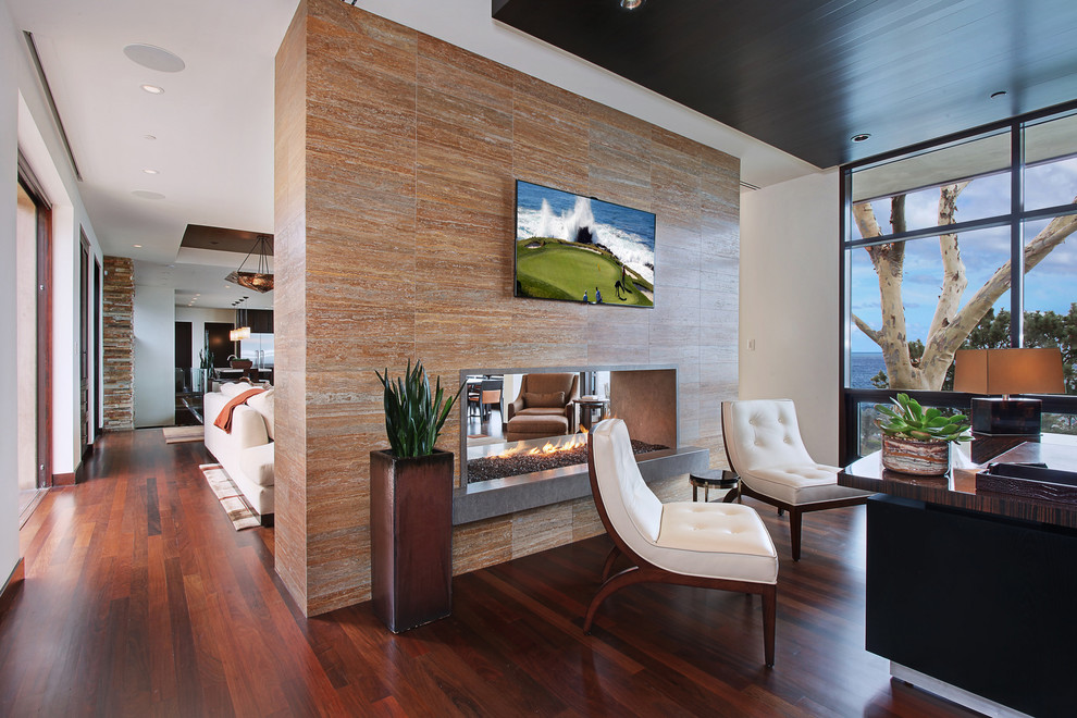 Photo of a large contemporary study room in Orange County with beige walls, dark hardwood floors, a two-sided fireplace, a tile fireplace surround, a freestanding desk and brown floor.