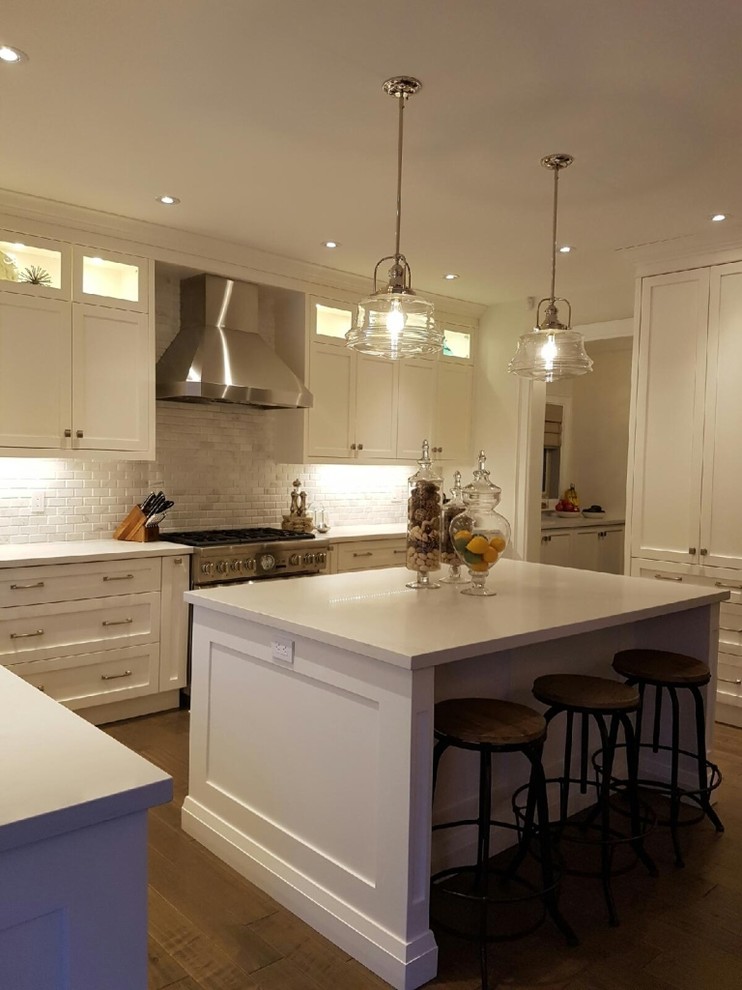 Mid-sized transitional l-shaped medium tone wood floor and brown floor open concept kitchen photo in Toronto with an undermount sink, beaded inset cabinets, white cabinets, solid surface countertops, white backsplash, brick backsplash, stainless steel appliances, an island and white countertops