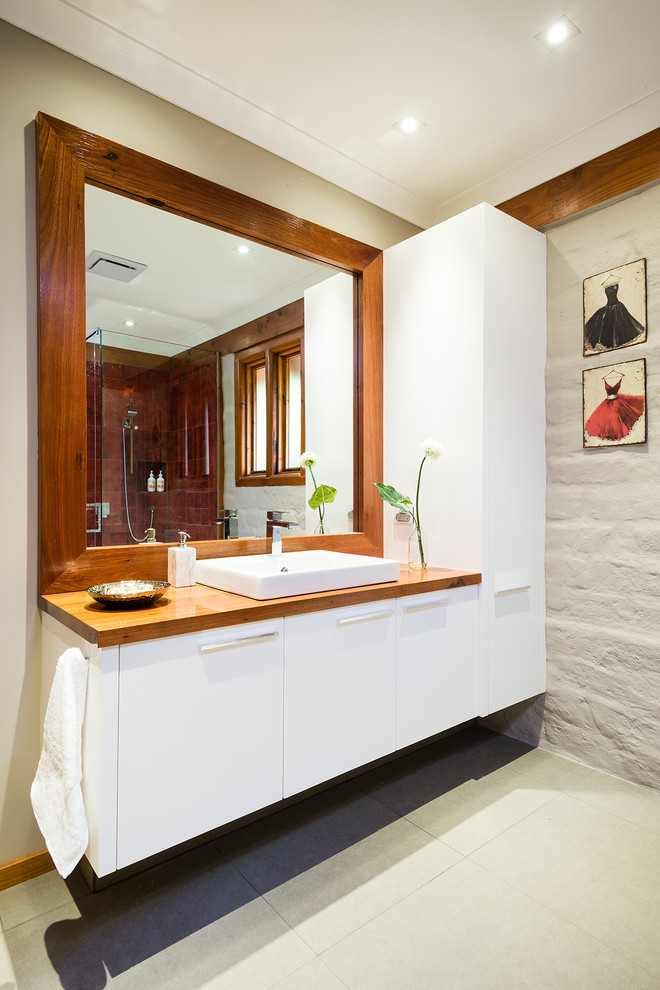 Photo of a mid-sized country master bathroom in Melbourne with wood benchtops, a corner shower, a one-piece toilet, red tile, ceramic tile, ceramic floors, beige walls and grey cabinets.