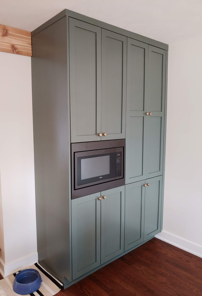 Inspiration for a mid-sized transitional l-shaped dark wood floor eat-in kitchen remodel with a farmhouse sink, recessed-panel cabinets, green cabinets, quartz countertops, white backsplash, black appliances, an island and white countertops