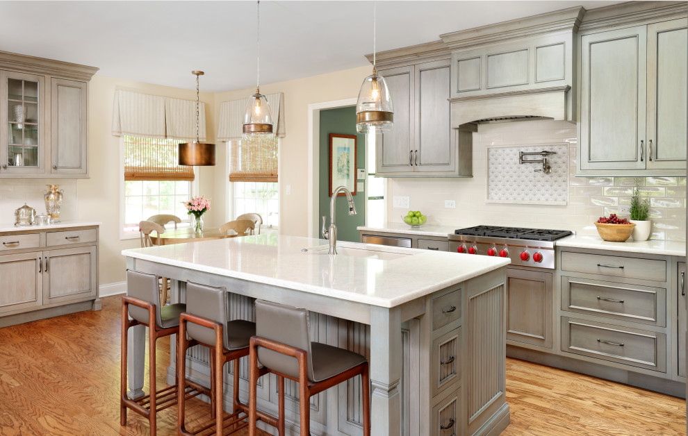 Klassisk inredning av ett stort vit vitt kök, med gröna skåp, bänkskiva i kvarts, en undermonterad diskho, vitt stänkskydd, stänkskydd i keramik, integrerade vitvaror, mellanmörkt trägolv, brunt golv och släta luckor
