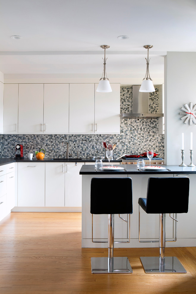 This is an example of a contemporary l-shaped separate kitchen in New York with an undermount sink, white cabinets, granite benchtops, multi-coloured splashback, mosaic tile splashback, panelled appliances, a peninsula and black benchtop.