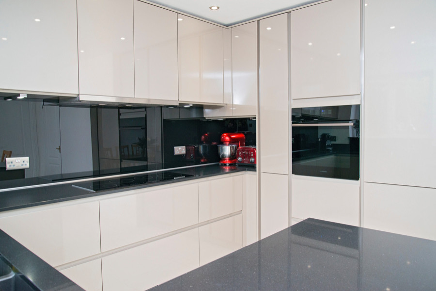 Photo of a mid-sized modern u-shaped eat-in kitchen in Other with a double-bowl sink, flat-panel cabinets, beige cabinets, granite benchtops, black splashback, glass sheet splashback, black appliances and black benchtop.