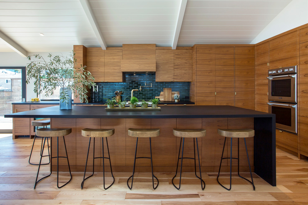 Contemporary galley kitchen in San Francisco with flat-panel cabinets, dark wood cabinets, black splashback, stainless steel appliances, light hardwood floors, with island and brown floor.