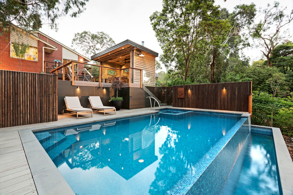 This is an example of a mid-sized contemporary backyard rectangular infinity pool in Melbourne with a pool house and tile.