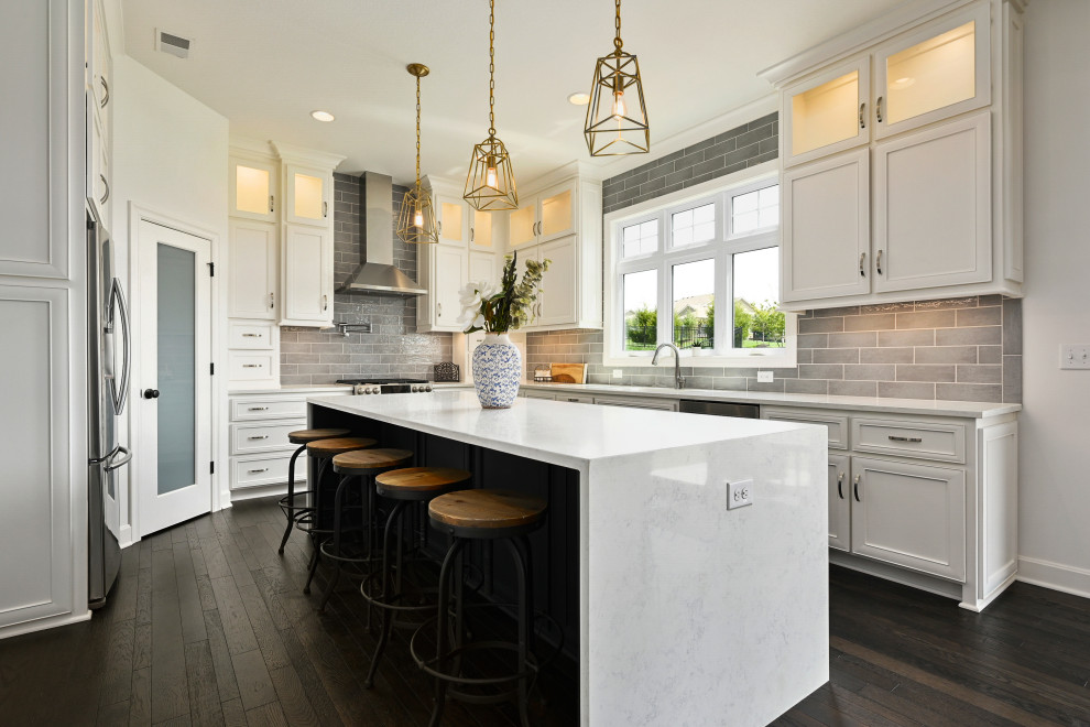 Inspiration for a transitional u-shaped kitchen in Kansas City with an undermount sink, recessed-panel cabinets, white cabinets, grey splashback, subway tile splashback, stainless steel appliances, dark hardwood floors, with island, brown floor and white benchtop.