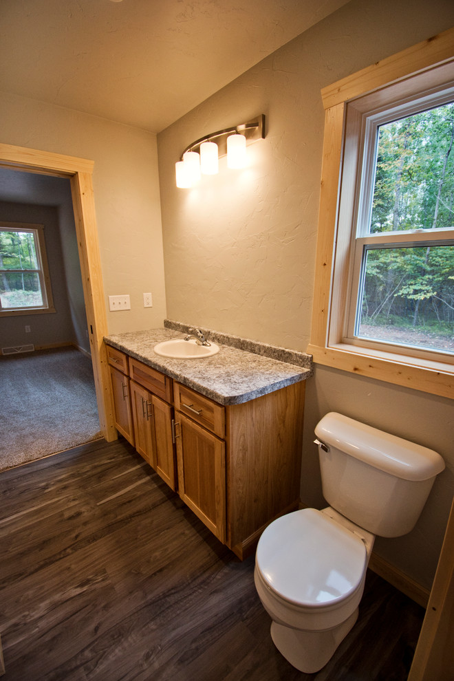 Example of a mid-sized mountain style master beige tile medium tone wood floor and brown floor bathroom design with recessed-panel cabinets, dark wood cabinets, a drop-in sink, laminate countertops and brown countertops