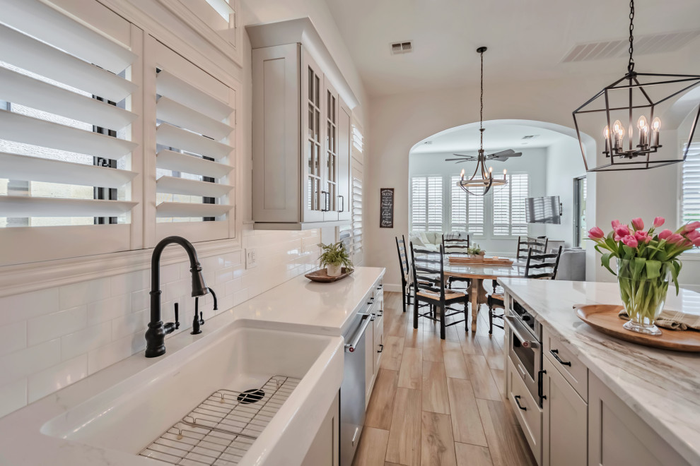 Inspiration for a large transitional u-shaped porcelain tile, brown floor and exposed beam kitchen remodel in Phoenix with a farmhouse sink, shaker cabinets, gray cabinets, quartzite countertops, white backsplash, porcelain backsplash, stainless steel appliances, an island and white countertops