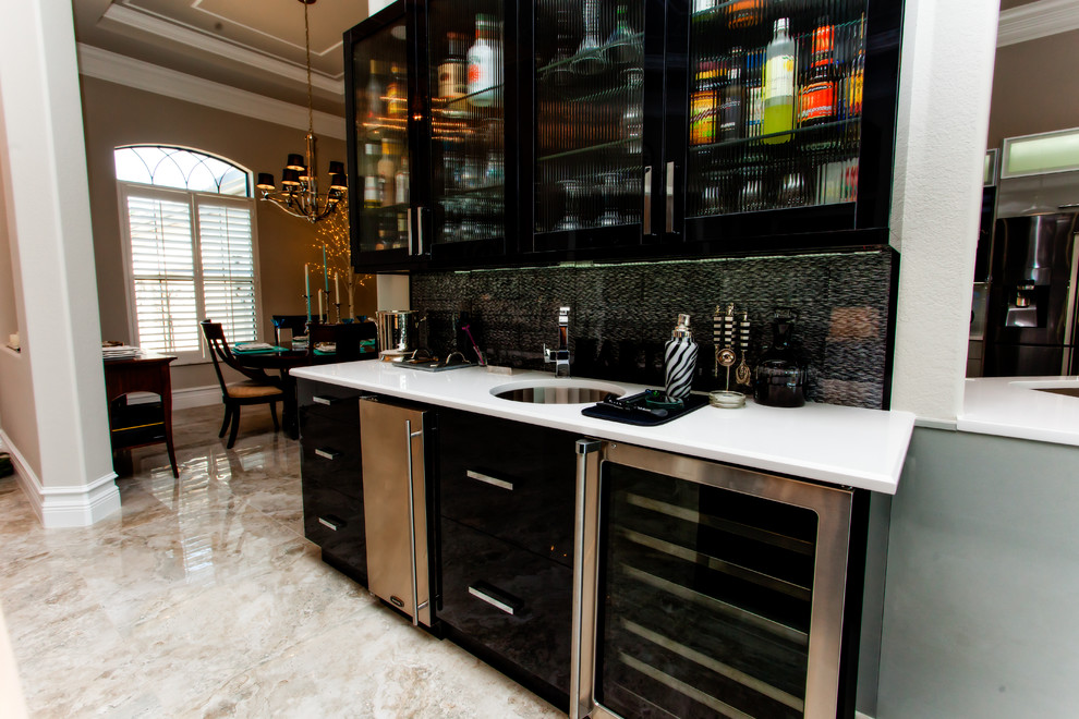 Photo of a mid-sized transitional single-wall wet bar in Miami with an undermount sink, glass-front cabinets, black cabinets, solid surface benchtops, multi-coloured splashback, marble floors and beige floor.