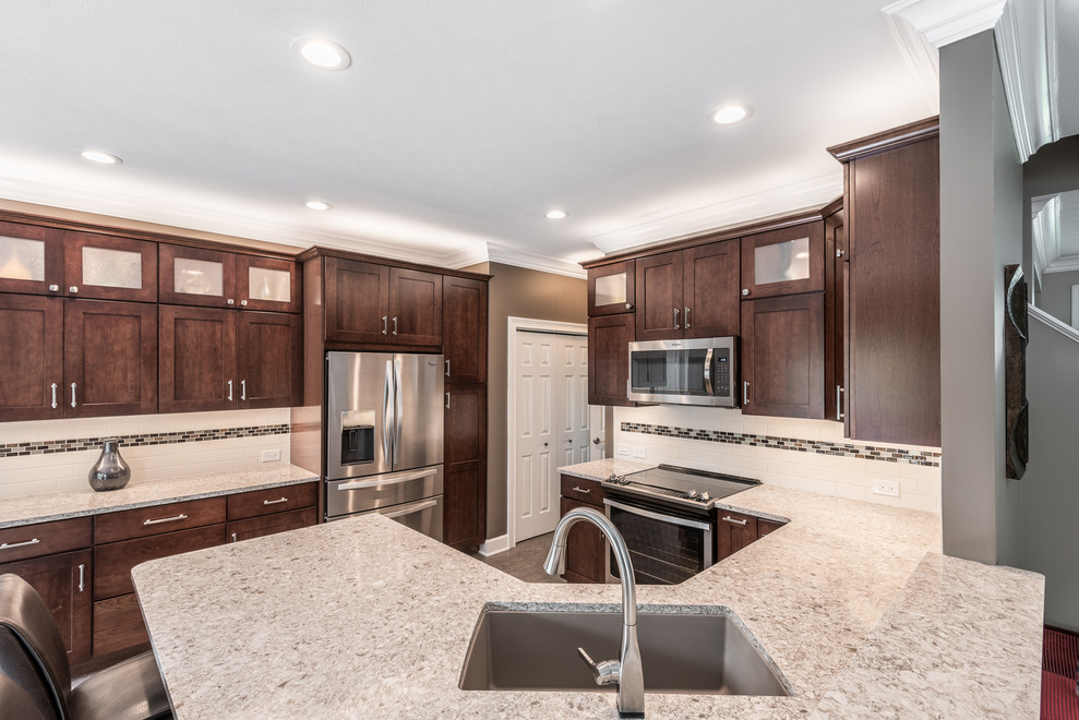 Inspiration for a mid-sized transitional u-shaped vinyl floor and brown floor kitchen remodel with an undermount sink, recessed-panel cabinets, brown cabinets, quartz countertops, multicolored backsplash, porcelain backsplash, stainless steel appliances, a peninsula and multicolored countertops