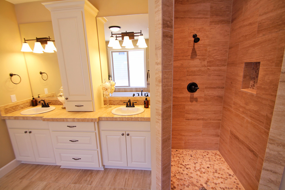 Inspiration for a mid-sized transitional master bathroom in Portland with raised-panel cabinets, white cabinets, a drop-in tub, an alcove shower, a one-piece toilet, beige tile, stone tile, beige walls, travertine floors, a drop-in sink and tile benchtops.