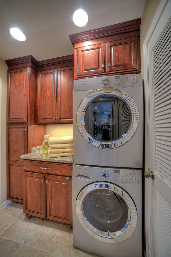 Small traditional single-wall laundry room in Other with an undermount sink, raised-panel cabinets, medium wood cabinets, granite benchtops, beige walls, porcelain floors and a stacked washer and dryer.