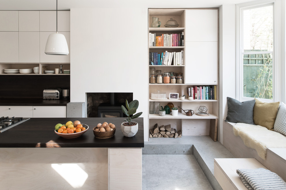 This is an example of a contemporary galley open plan kitchen in London with flat-panel cabinets, white cabinets, concrete floors, with island, grey floor, black benchtop and black splashback.