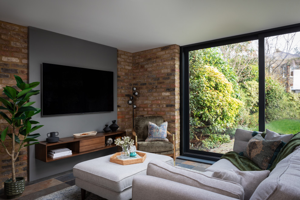 This is an example of a contemporary living room in London with grey walls, a wall mounted tv, multi-coloured floors and brick walls.