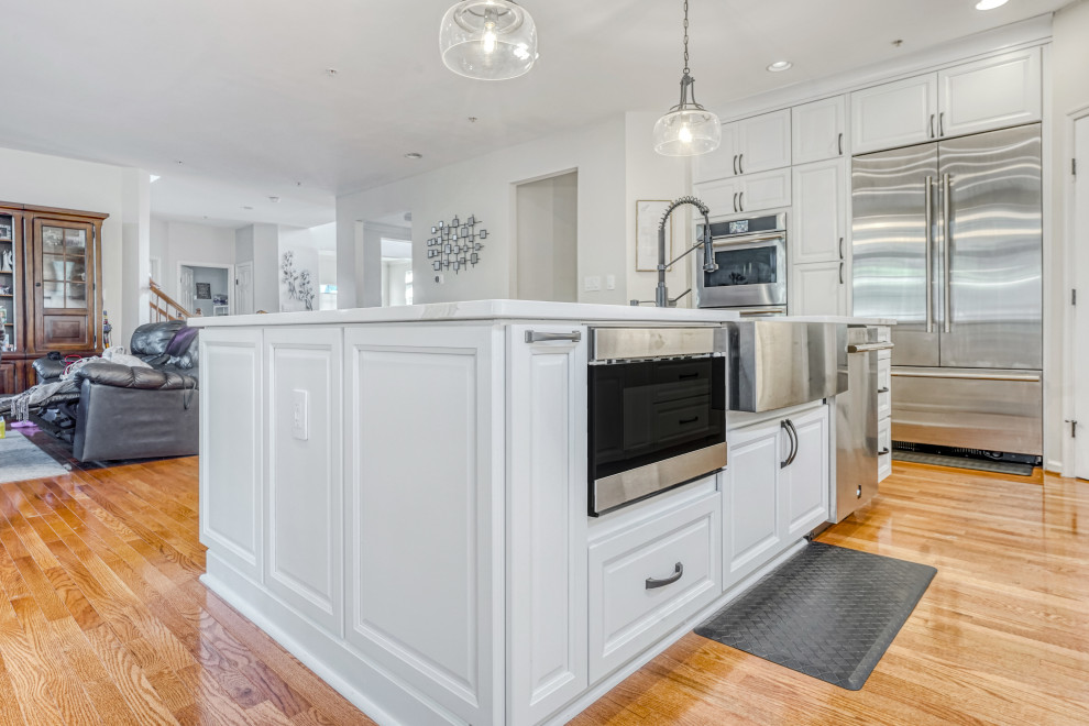 This is an example of an expansive classic l-shaped open plan kitchen in DC Metro with raised-panel cabinets, white cabinets, engineered stone countertops, white splashback, metro tiled splashback, stainless steel appliances, an island and a belfast sink.