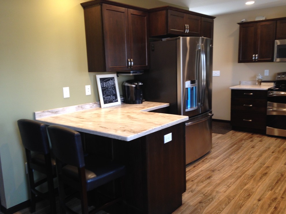 Mid-sized mountain style kitchen photo with an integrated sink, flat-panel cabinets, dark wood cabinets, solid surface countertops, stainless steel appliances and a peninsula