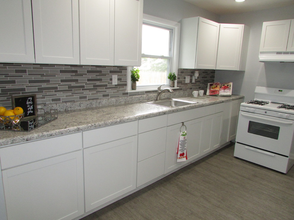 Inspiration for a transitional single-wall kitchen in Indianapolis with a single-bowl sink, shaker cabinets, white cabinets, laminate benchtops, metallic splashback, glass tile splashback, white appliances, vinyl floors, grey floor and grey benchtop.