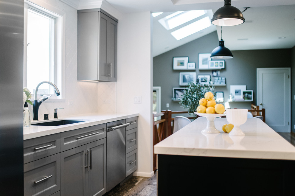 Photo of a mid-sized contemporary u-shaped eat-in kitchen in San Francisco with a farmhouse sink, shaker cabinets, grey cabinets, quartz benchtops, white splashback, ceramic splashback, stainless steel appliances, laminate floors, with island and brown floor.