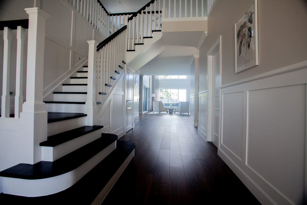 На фото: большая п-образная лестница в классическом стиле с деревянными ступенями, крашенными деревянными подступенками, деревянными перилами и панелями на стенах с