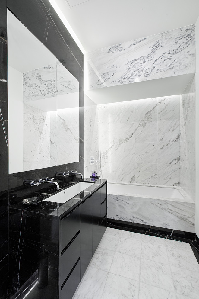 Contemporary bathroom in New York with a trough sink, flat-panel cabinets, black cabinets, an alcove tub, black tile and stone slab.