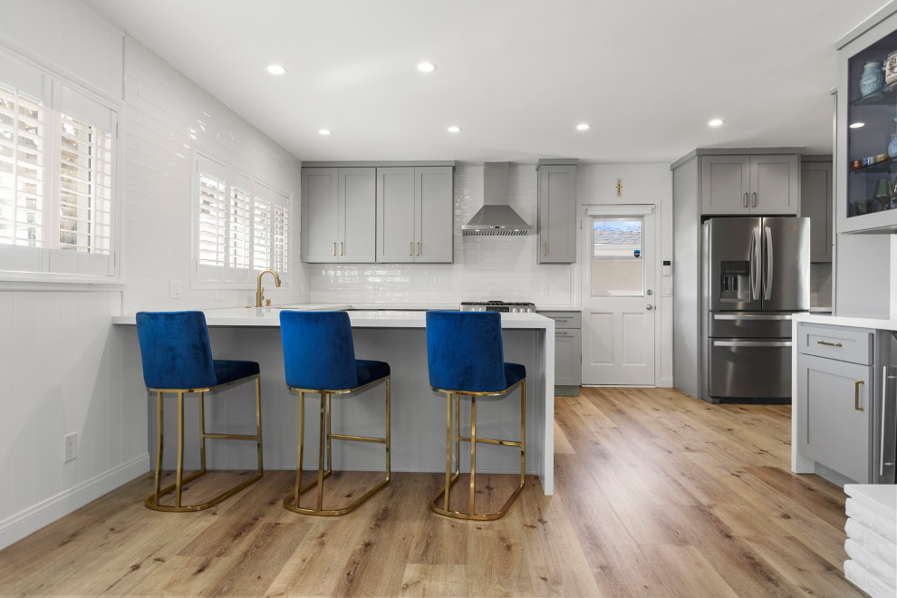 Design ideas for a mid-sized modern u-shaped separate kitchen in Los Angeles with a drop-in sink, shaker cabinets, grey cabinets, marble benchtops, white splashback, subway tile splashback, stainless steel appliances, light hardwood floors, no island, brown floor and white benchtop.