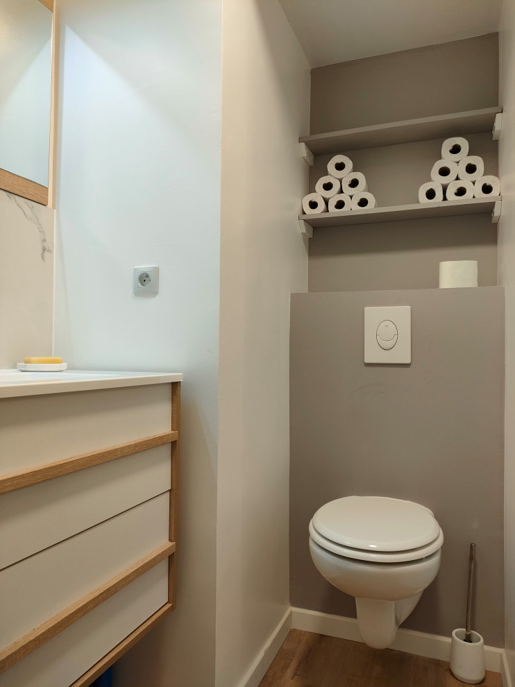 Design ideas for a small contemporary cloakroom in Strasbourg with flat-panel cabinets, white cabinets, a wall mounted toilet, white tiles, marble tiles, beige walls, light hardwood flooring, a trough sink, glass worktops, brown floors, white worktops and a floating vanity unit.