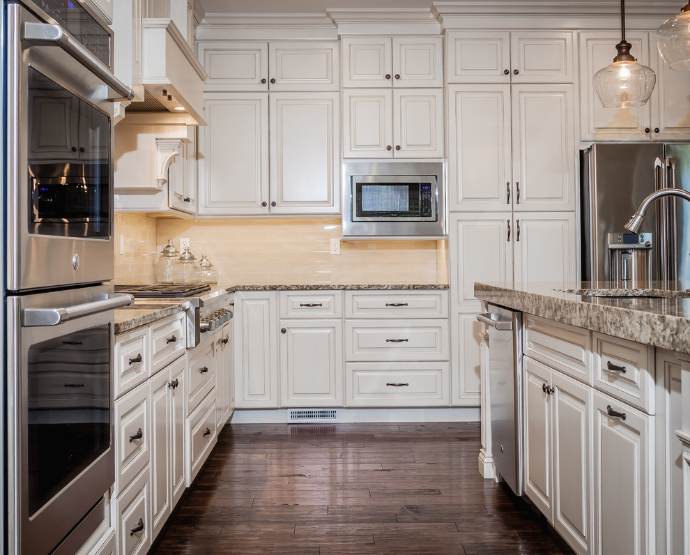 Example of a large transitional l-shaped kitchen design in St Louis with an undermount sink, raised-panel cabinets, white cabinets, granite countertops, beige backsplash, subway tile backsplash, stainless steel appliances and an island