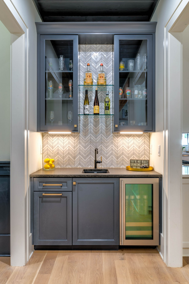 Photo of a small country single-wall wet bar in Atlanta with an undermount sink, shaker cabinets, grey cabinets, granite benchtops, white splashback, marble splashback, light hardwood floors, white floor and black benchtop.