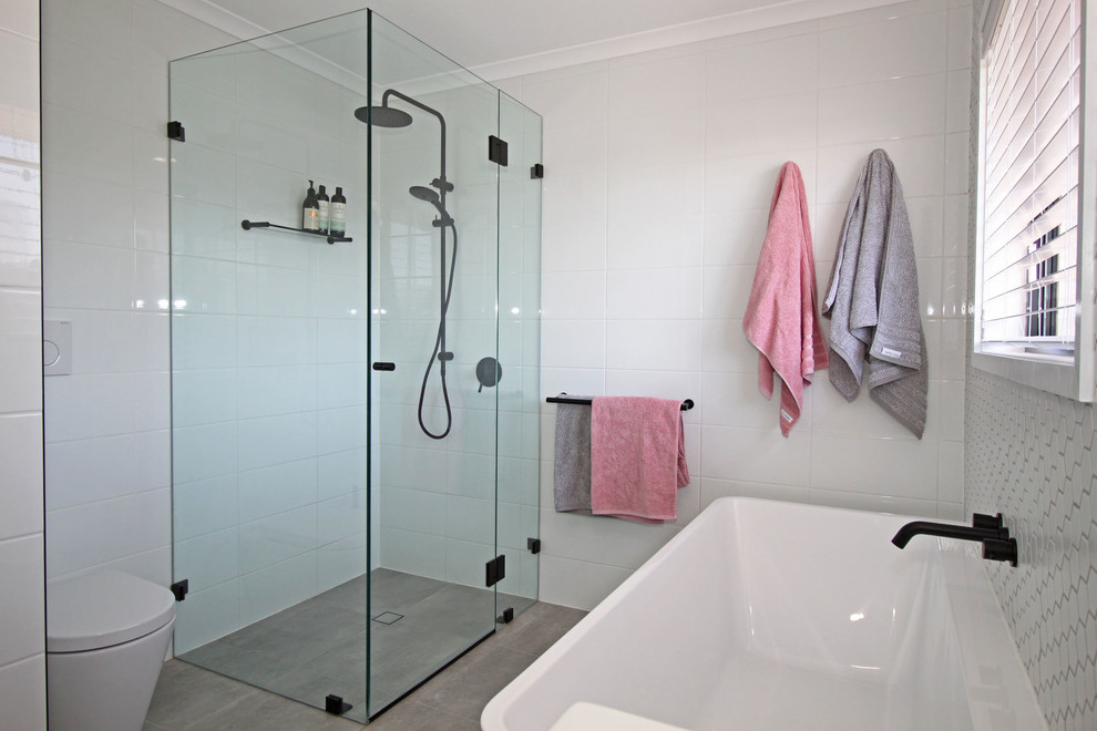 Design ideas for a small modern kids bathroom in Brisbane with flat-panel cabinets, light wood cabinets, a freestanding tub, a curbless shower, a wall-mount toilet, white tile, ceramic tile, white walls, porcelain floors, an integrated sink, solid surface benchtops, grey floor, a hinged shower door and white benchtops.