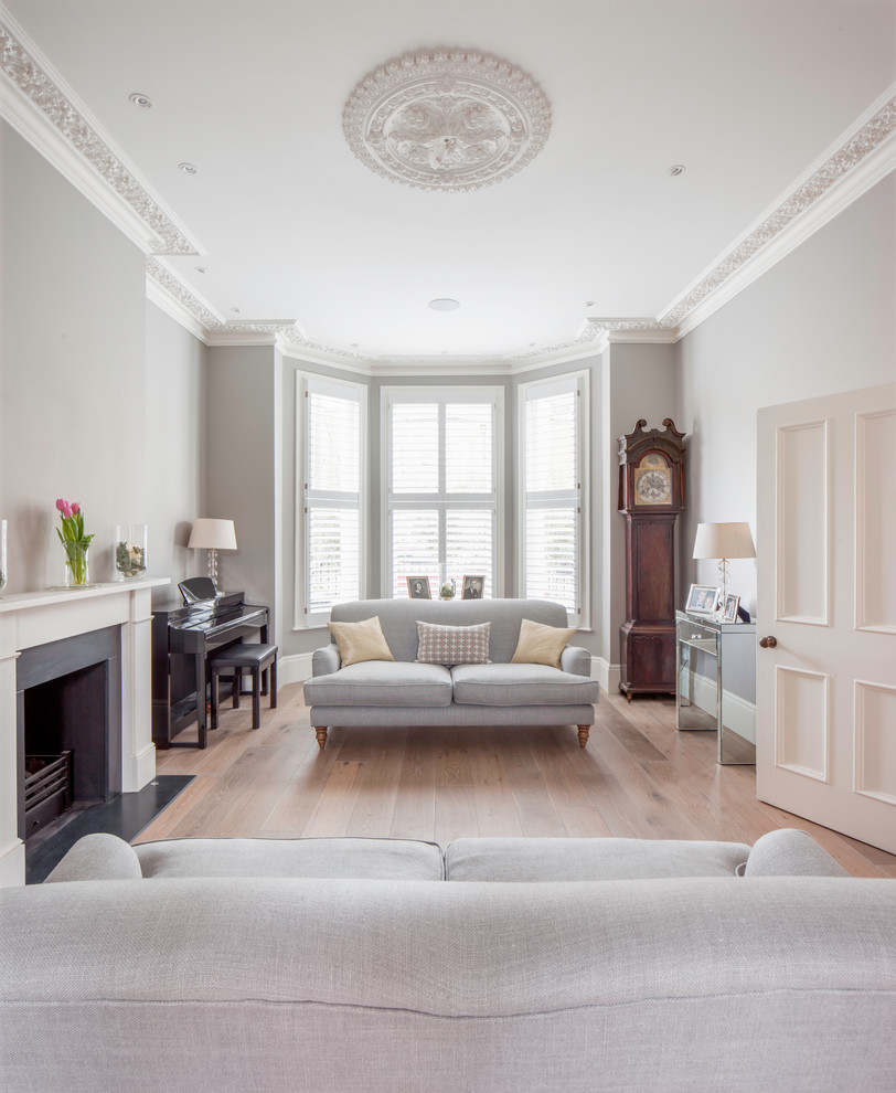 Inspiration for a mid-sized transitional enclosed living room in London with grey walls, light hardwood floors, a standard fireplace and beige floor.